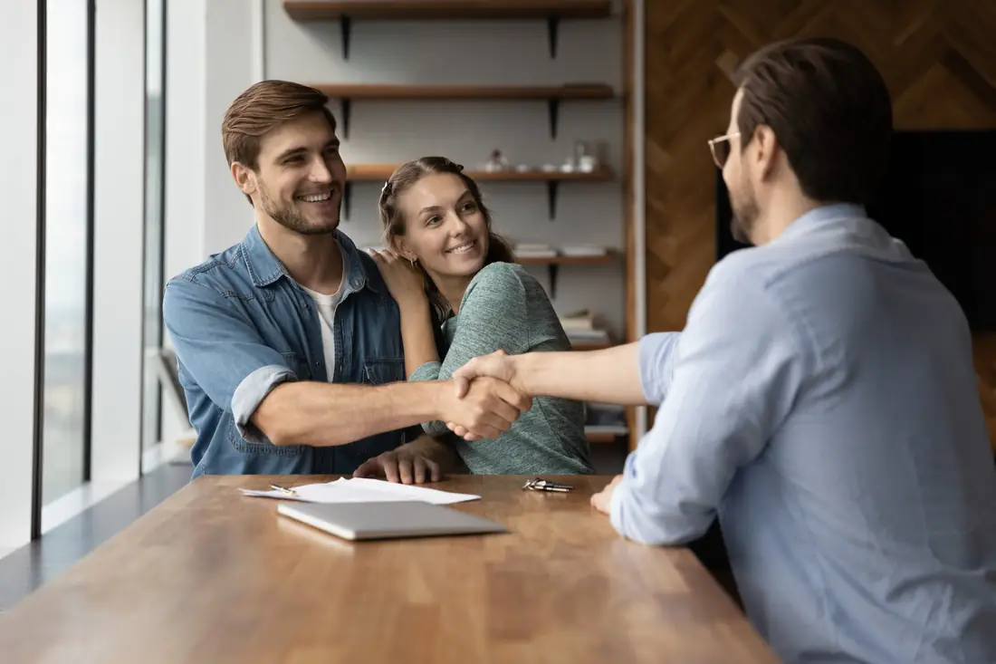 Young couple shaking hands with their solicitor across a desk