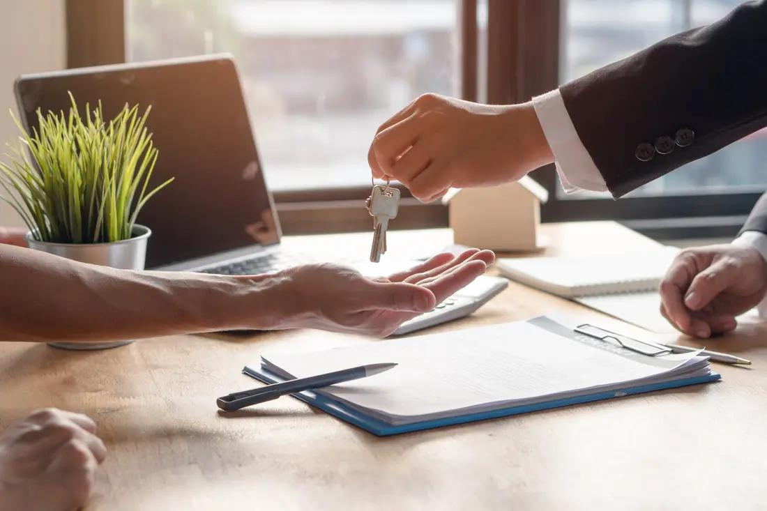 House keys being handed over across a desk with a signed contract